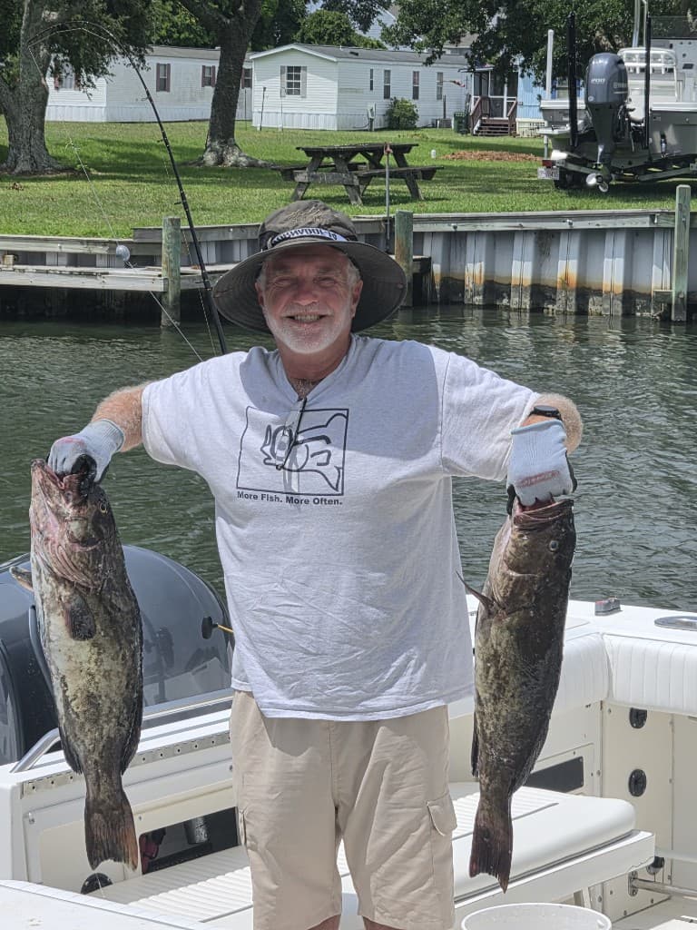 A smiling guest on a boat holding two large fish after a day on the water